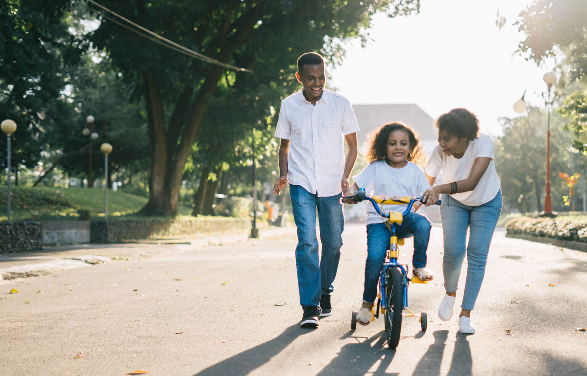 An image of a family with young daughter learning to ride a bike.